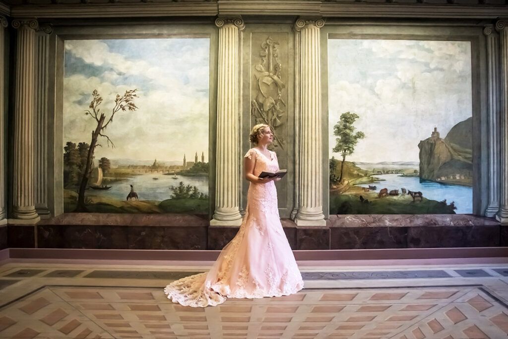 Auf dem Bild ist unser Model im Tapetenzimmer in Stralsund zu sehen, stehend vor den originalen, handgemalten Tapeten aus dem 18. Jahrhundert. Die historische Kulisse mit ihren feinen Linien, floralen Ornamenten und der stillen Patina vergangener Jahrhunderte bildet einen außergewöhnlichen Rahmen für dieses moderne, bewusst reduzierte Portrait. Das Mazelle Photography Fotostudio® erhielt die seltene und besondere Gelegenheit, in diesem kulturhistorisch bedeutenden Raum ein exklusives Fotoshooting durchzuführen. Die Verbindung aus barocker Wandkunst und klarer, zeitloser Bildsprache macht diese Aufnahme zu einem einzigartigen Zusammenspiel aus Geschichte, Ästhetik und fotografischer Präzision.