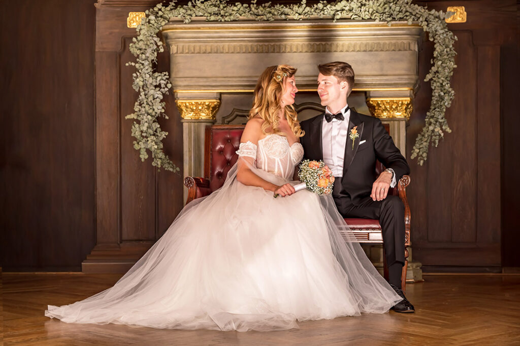 Das Bild zeigt ein Brautpaar im Schlosshotel Ralswiek auf der Insel Rügen, sitzend vor dem alten, historischen Kamin des Hauses. Die Szene verbindet die intime Ruhe des Moments mit der charaktervollen Architektur des Schlosses.